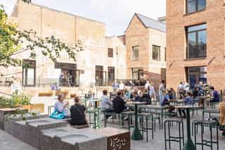 Photograph showing people sat on benches, eating and drinking in an outdoor area.