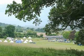 An image of the Camp Standish setting, with all the tents and the Standish Studio in the distance