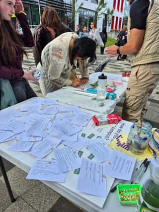 An outdoor consultation event at a University campus. Students are seen attaching notes to a board, and taking part in a clay workshop