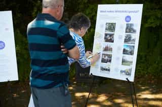 An elderly couple at an outdoor consultation event. They are sticking post it notes on a board