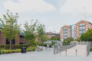 Where the David Oluwale bridge meets the road. There is a handrail on the exit and small bollards. New trees and planting surrounds the bridge exit.