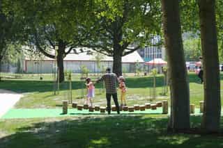 An image of a father helping his two daughters across the playing equipment at Ancoats Green