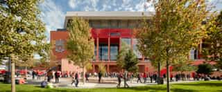 A photo looking over a grassed area to Anfield stadium, with street trees in the shot and fans stood around.