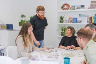 An image of people sat around a table smiling, a man stands over them as they discuss the plans on the table