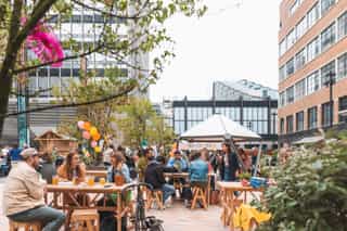 Image of people gathered in Sadler's Yard, NOMA for a summer party. People are sat at tables with balloons and bright decoration.