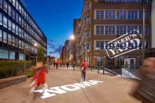 Night time image of the light displays at Sadler's Yard, which display the NOMA logos lit on the ground and the buildings opposite.