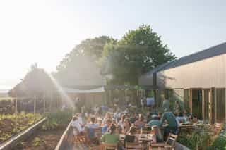 An image of people gathered outside sitting down at long tables, a ray of light shines down from the top left corner