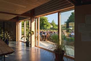 A wide angle image looking through full wall windows and doors, looking out at rows of people sat at various tables