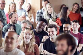 An image of a group of people sat in rows, laughing along to an unseen presenter