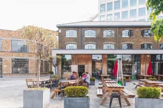 An image of four people drinking at a bench outside in a courtyard