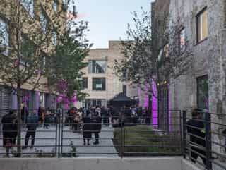 An image of the courtyard in Sugar House Island in use for an event, purple lighting against the walls and people networking