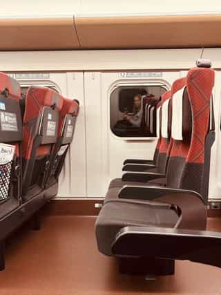 An POV image sitting on a train, the reflection of the photographer appears in the opposite window.