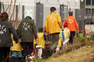 An image of people wearing different coloured jackets with the PLANT logo on the back, they are walking along a narrow path with kids